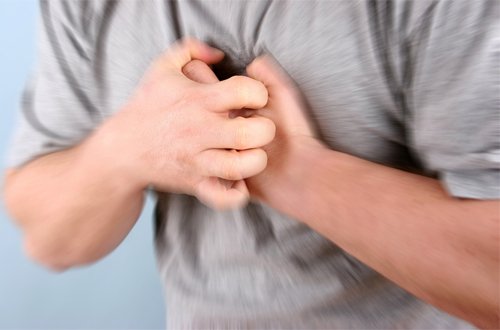 Một người đàn ông trung niên ôm ngực vì đau thắt ngực một triệu chứng có thể liên quan đến rối loạn nhịp tim