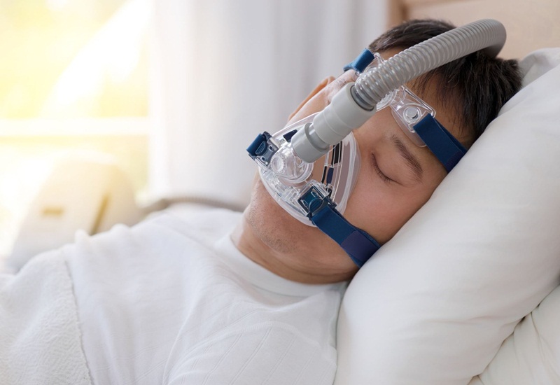 Bác sĩ đang điều chỉnh máy thở không xâm nhập NIV cho bệnh nhân đảm bảo mặt nạ vừa vặn và bệnh nhân thoải mái đồng thời theo dõi các chỉ số sinh tồn để phát hiện sớm các dấu hiệu bất thường